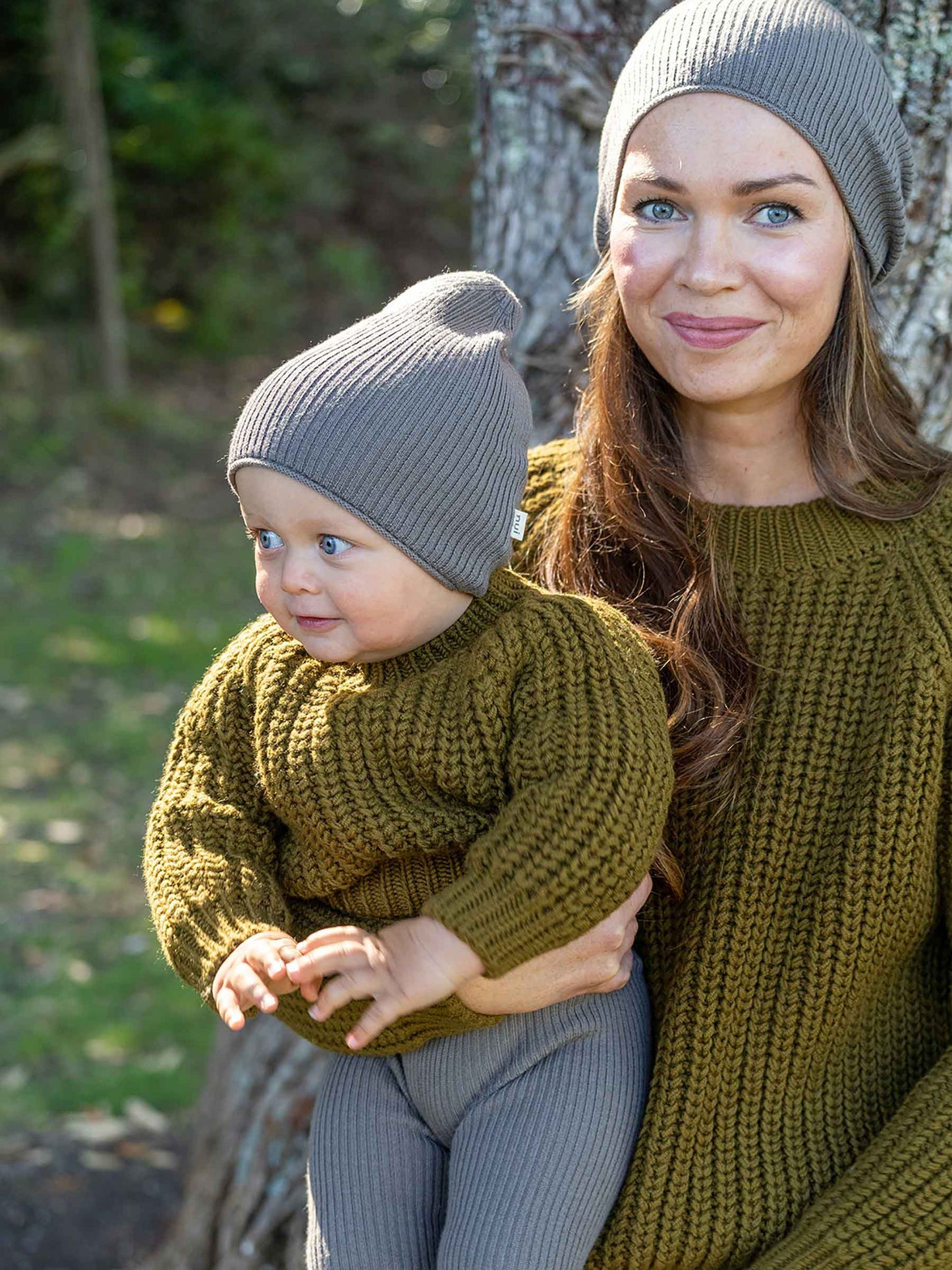 Nui Organics Women's Fishline Sweater in Kelp — mother and baby wearing matching chunky olive merino knit sweaters and grey beanies outdoors