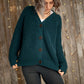 Nui Organics Women's Bernard Cardigan in Deep Sea — woman in chunky teal merino cardigan with corozo buttons and grey leggings against a wooden wall with fairy lights