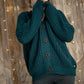 Nui Organics Women's Bernard Cardigan in Deep Sea — close-up of chunky teal merino knit and corozo nut buttons against a wooden backdrop with fairy lights