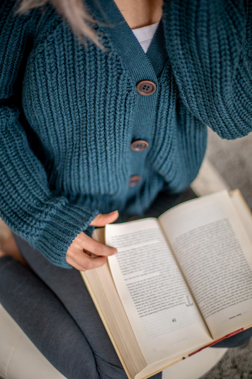 Nui Organics Women's Bernard Cardigan in Deep Sea — close-up of corozo nut button detail on chunky teal merino cardigan with open book in lap