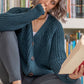 Nui Organics Women's Bernard Cardigan in Deep Sea — woman in chunky teal merino cardigan reading a book in front of a bookshelf