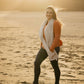 Nui Organics Women's Knit Leggings in Charcoal — woman wearing charcoal merino leggings with rust top and natural wrap on a sandy beach at sunset
