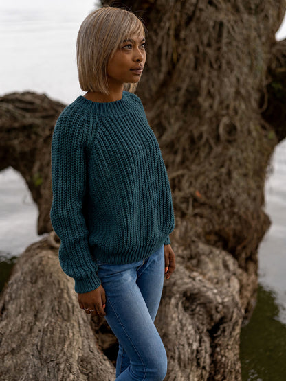 Nui Organics Women's Fishline Sweater in Deep Sea — close-up of chunky teal merino knit sweater with raglan sleeves and ribbed cuffs, worn with jeans outdoors