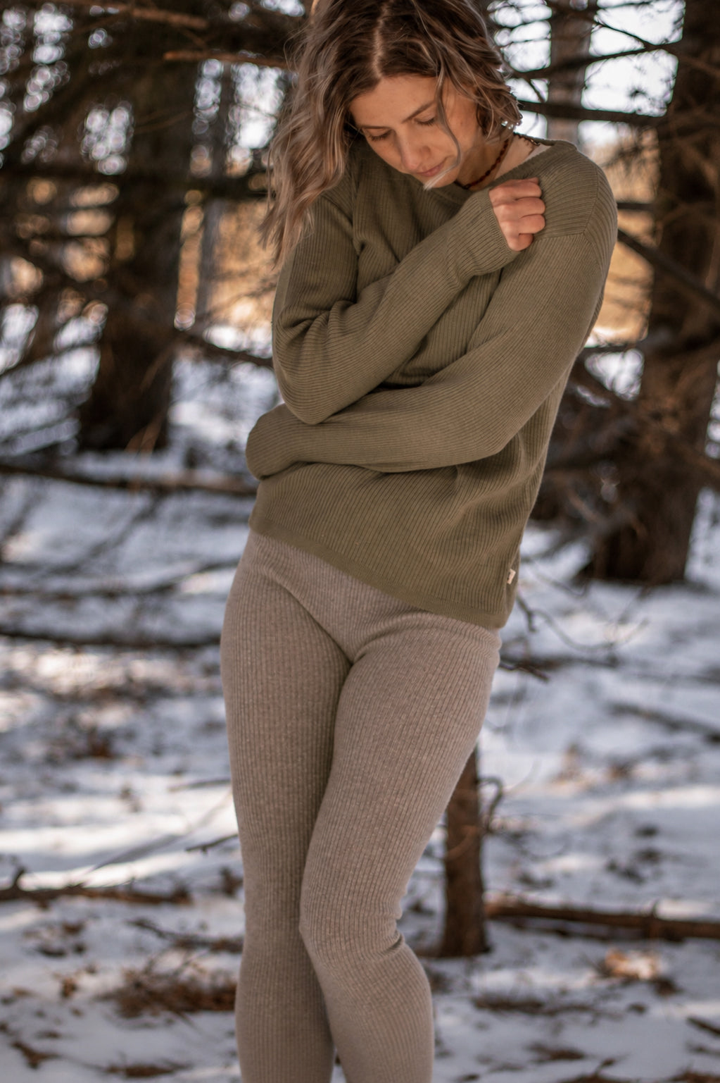 Nui Organics Women's Knit Leggings in Sparrow — woman in sparrow rib knit merino leggings and olive sweater in a snowy winter forest