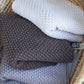 Nui Organics Koha Merino Baby Blanket - three textured knit merino wool blankets in Oatmeal, Cocoa and Silver folded in a wicker basket.