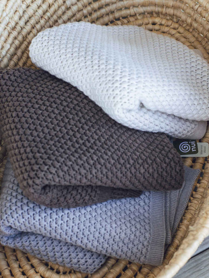 Nui Organics Koha Merino Baby Blanket - three textured knit merino wool blankets in Oatmeal, Cocoa and Silver folded in a wicker basket.