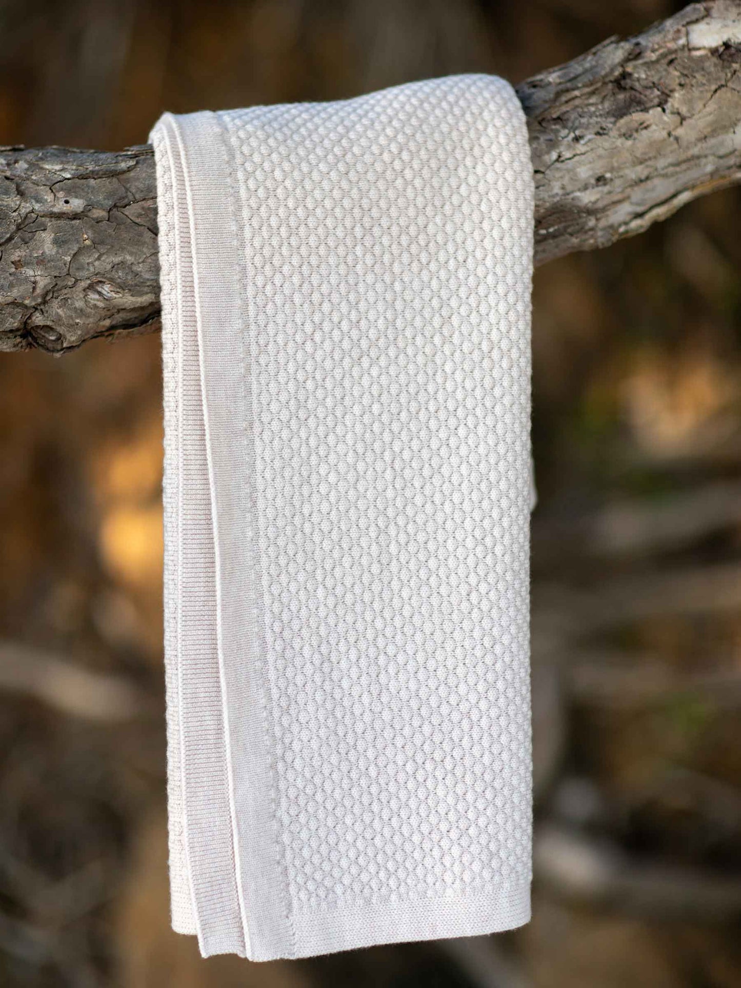 Nui Organics Koha Merino Baby Blanket in Oatmeal — textured knit 100% merino wool baby blanket folded over a branch outdoors