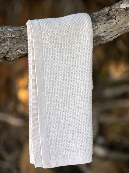Nui Organics Koha Merino Baby Blanket in Oatmeal — textured knit 100% merino wool baby blanket folded over a branch outdoors