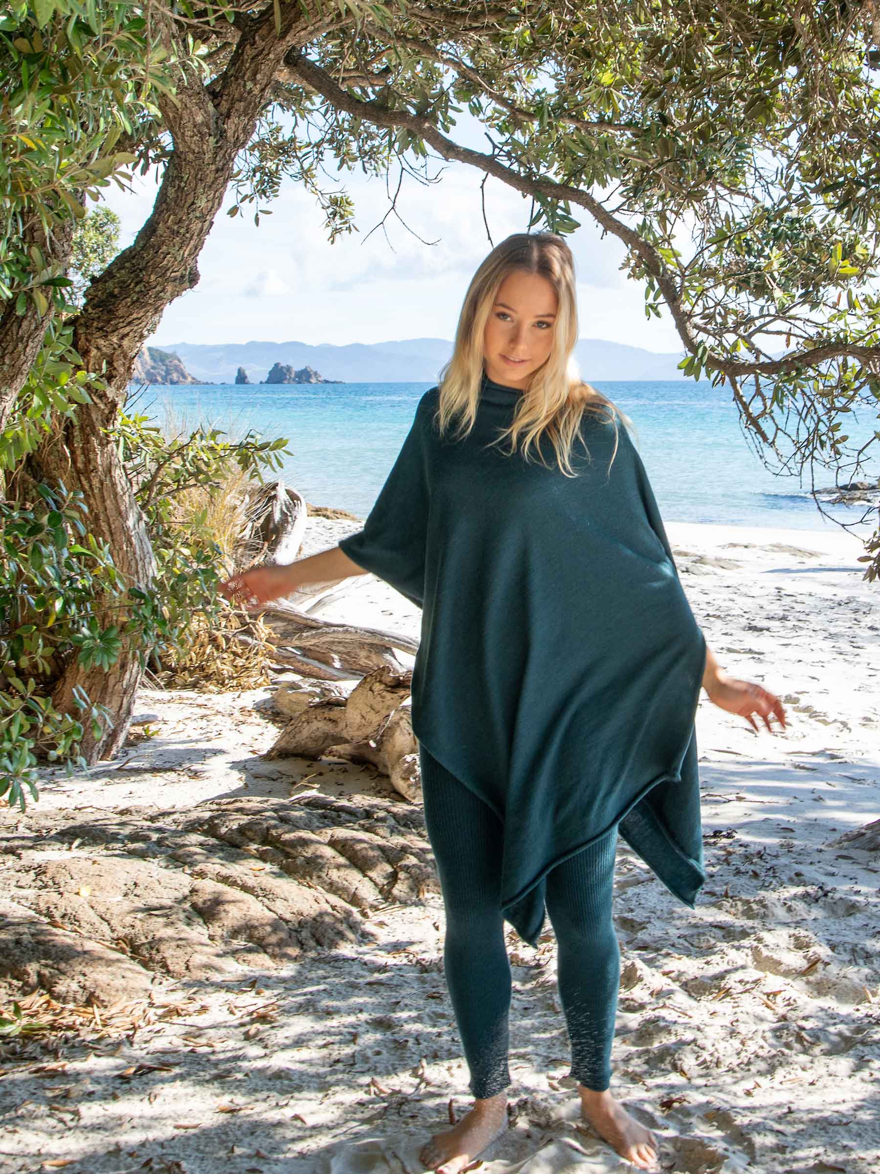 Nui Organics Women's Knit Leggings in Teal — woman wearing teal rib knit merino leggings and matching poncho on a sandy New Zealand beach