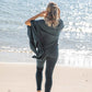 Nui Organics Women's Knit Leggings in Teal — rear view of woman in teal rib knit merino leggings and poncho walking barefoot toward the ocean