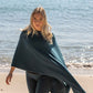 Nui Organics Women's Knit Leggings in Teal — woman in teal merino leggings and poncho walking barefoot along a sparkling beach shoreline