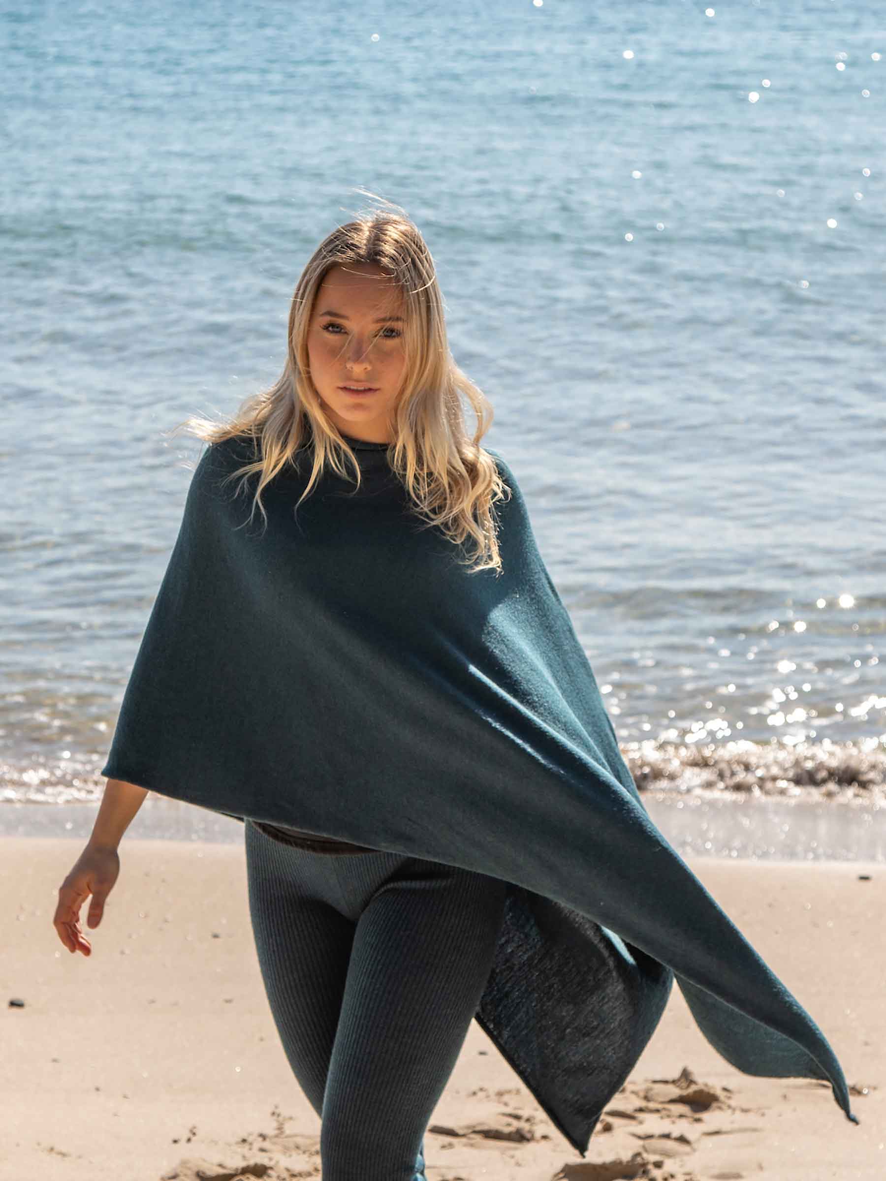 Nui Organics Women's Knit Leggings in Teal — woman in teal merino leggings and poncho walking barefoot along a sparkling beach shoreline