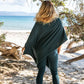 Nui Organics Women's Knit Leggings in Teal — rear view of woman in teal merino leggings and poncho on a sunny beach with coastal trees