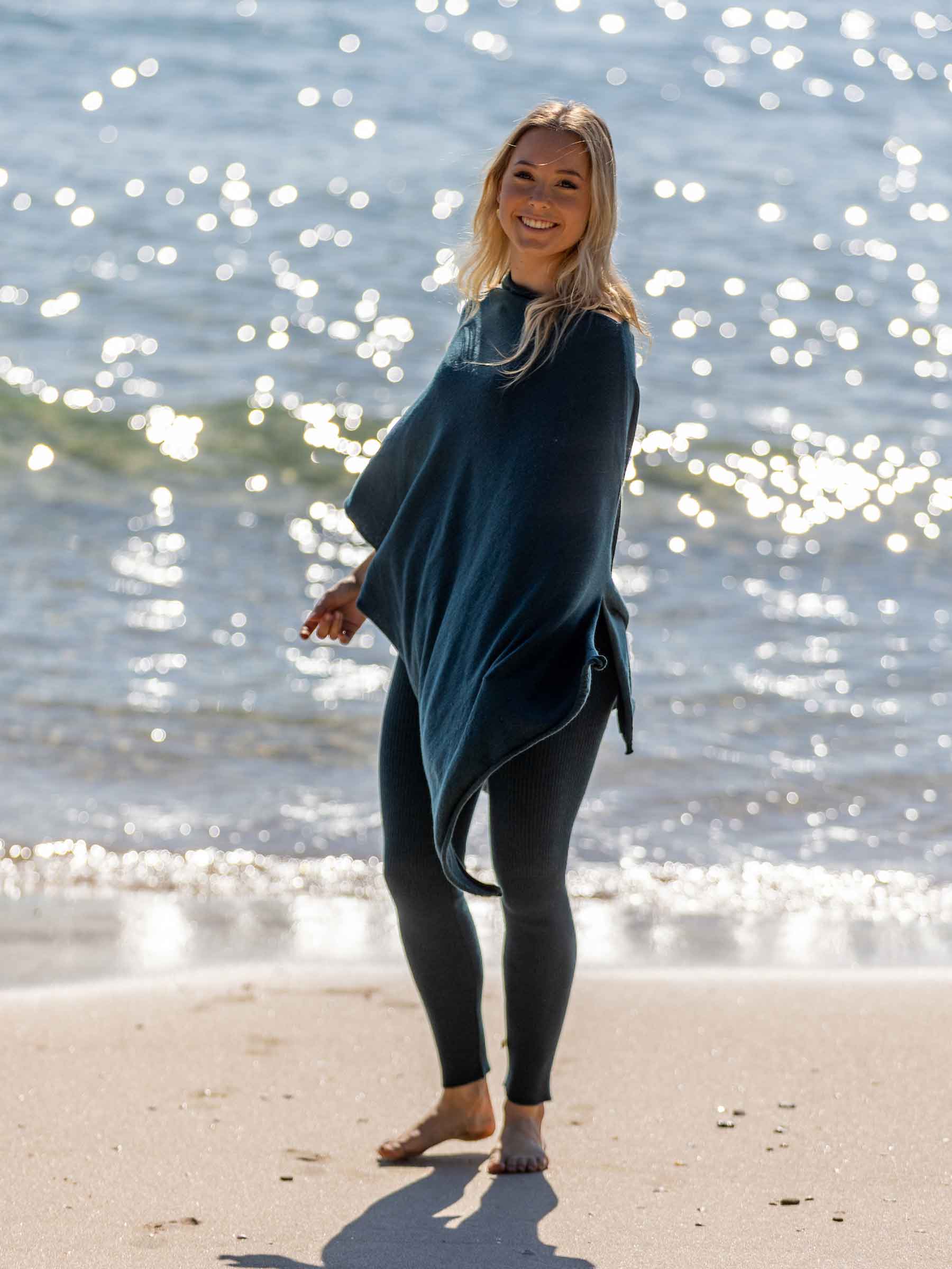 Nui Organics Women's Knit Leggings in Teal — smiling woman in teal merino leggings and poncho standing barefoot on a sunny beach