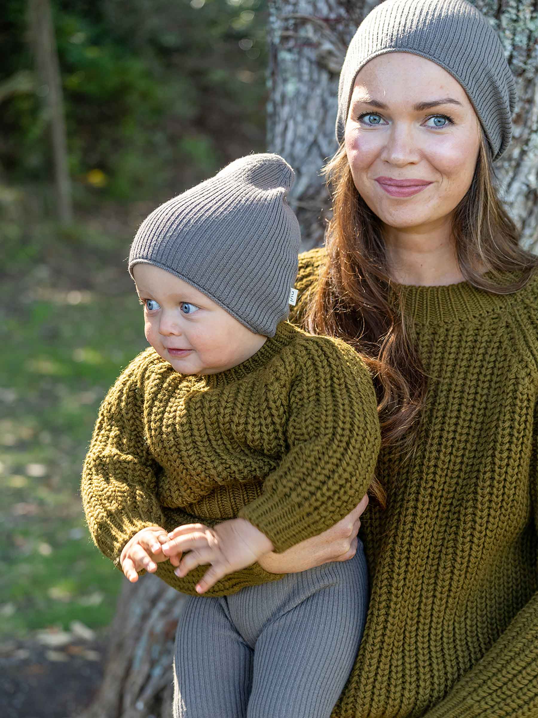 Nui Organics Women's Fishline Sweater in Kelp — mother and baby wearing matching chunky olive merino knit sweaters and grey beanies outdoors