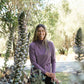 Woman in a purple wool sweater standing among tall plants in a natural setting