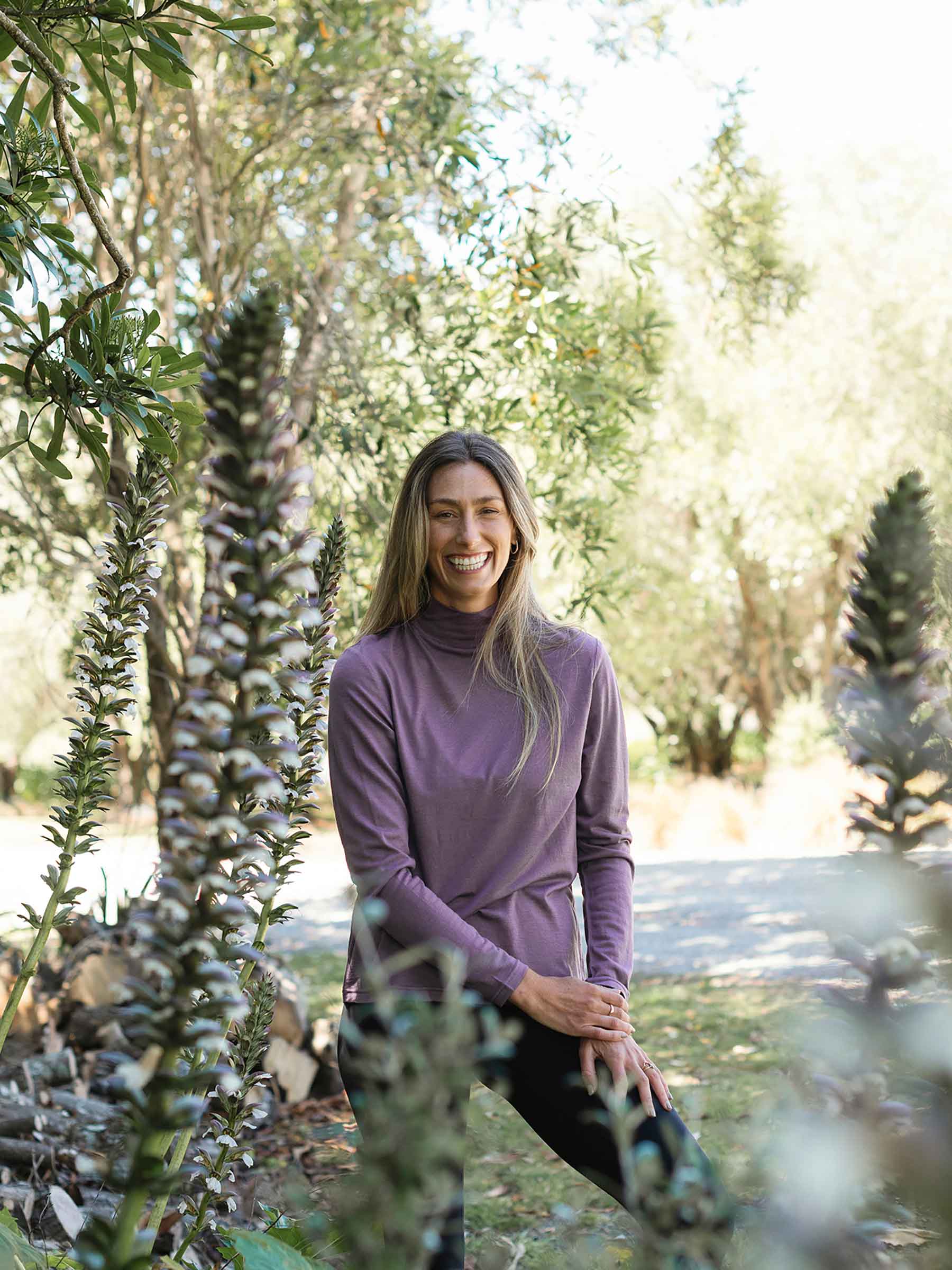 Woman in a purple wool sweater standing among tall plants in a natural setting
