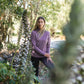Woman in a purple merino shirt standing among trees and plants
