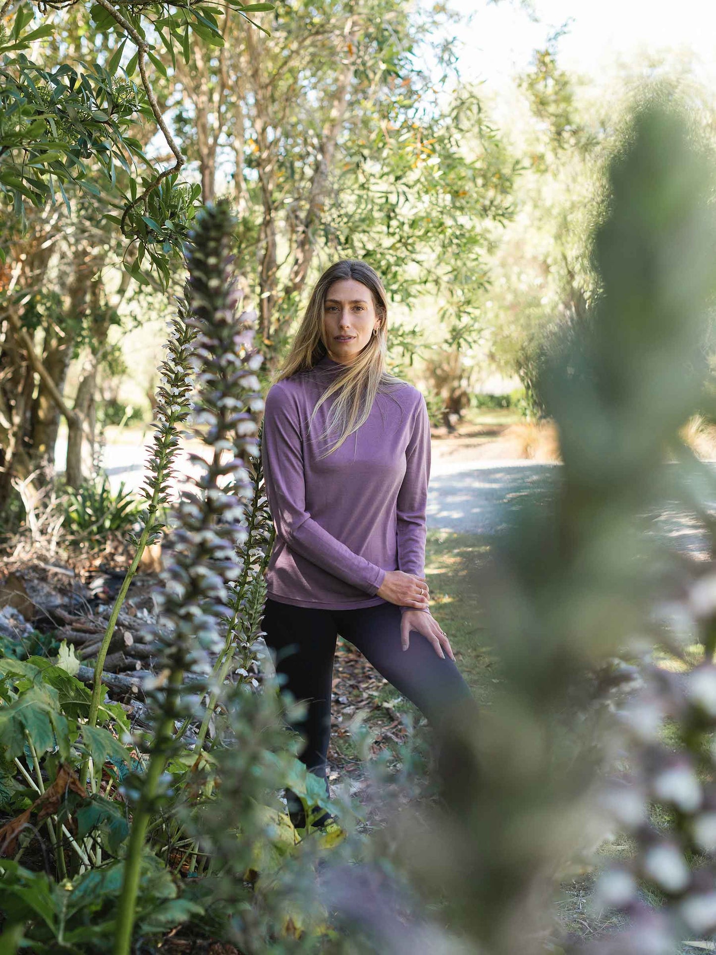 Woman in a purple merino shirt standing among trees and plants