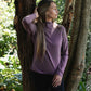 Woman in a purple long-sleeve shirt standing between two trees in a garden.
