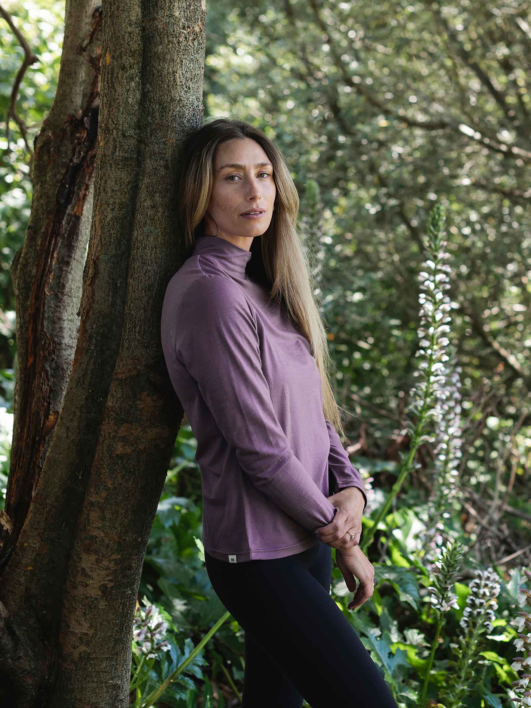 Woman in a purple jacket standing next to a tree in a forest