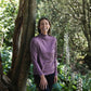 Woman in a purple long-sleeve shirt standing next to a tree in a forest