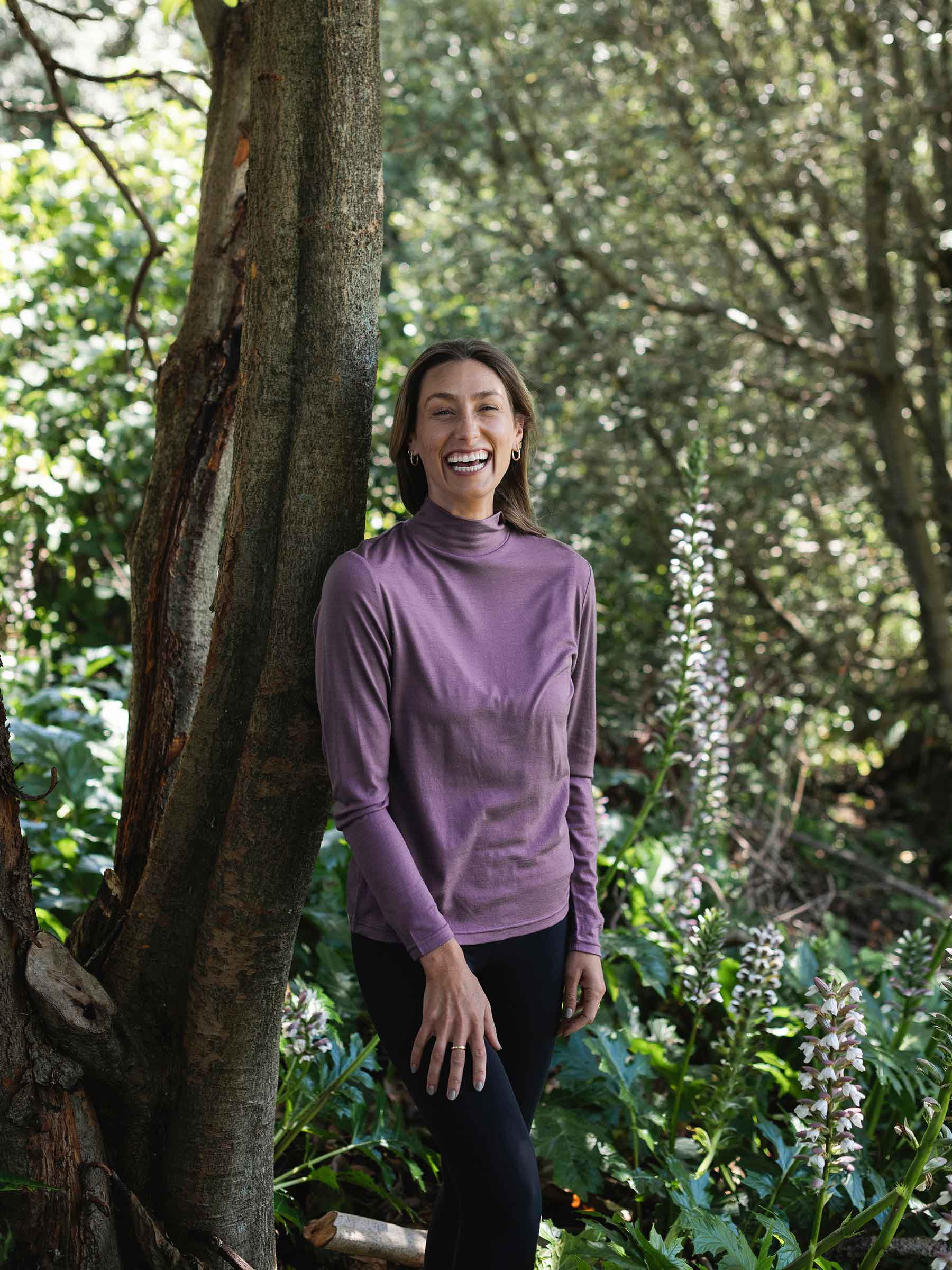 Woman in a purple long-sleeve shirt standing next to a tree in a forest