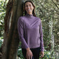 Woman wearing a purple long-sleeve shirt standing next to a tree in a forest