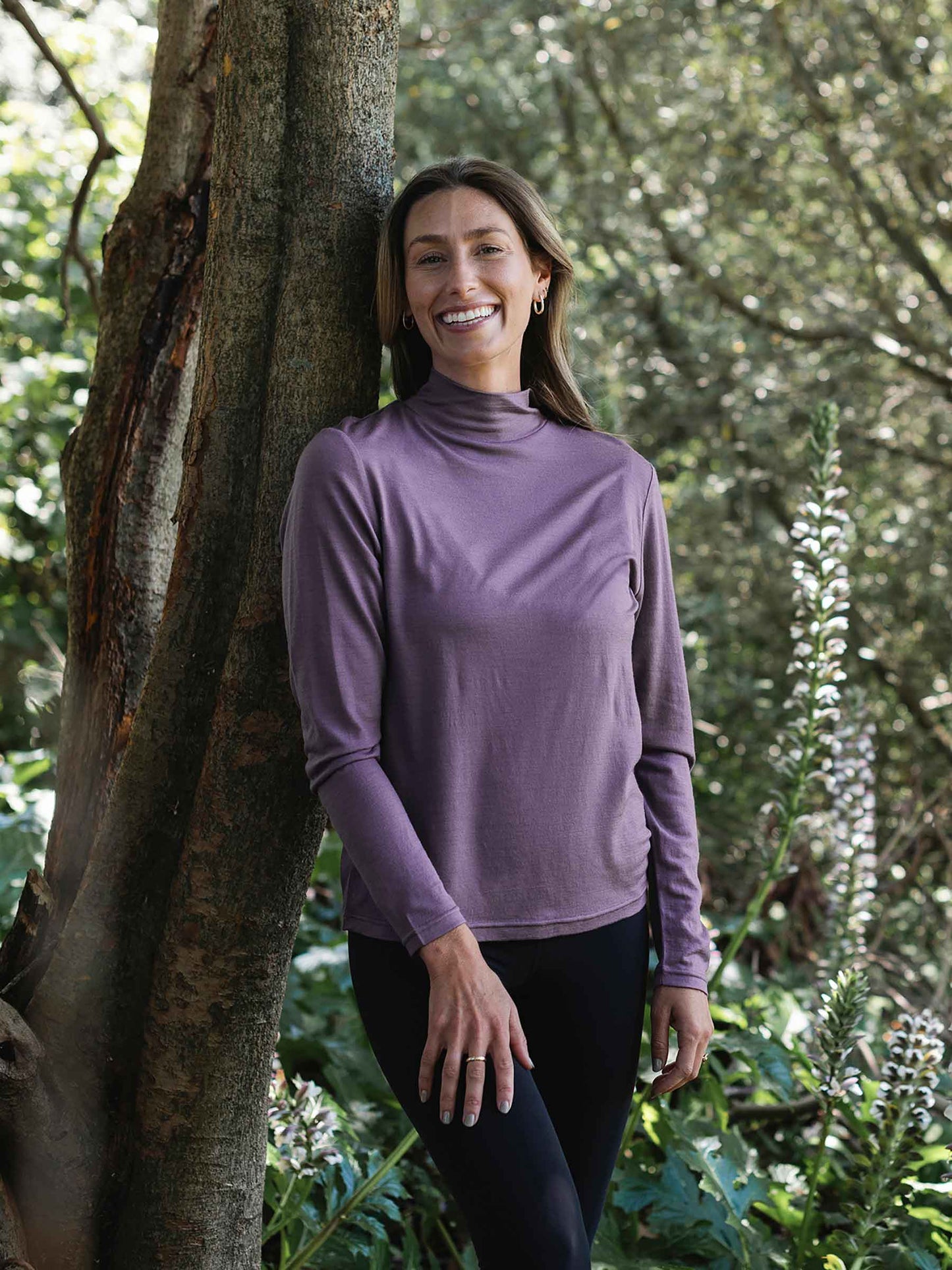 Woman wearing a purple long-sleeve shirt standing next to a tree in a forest